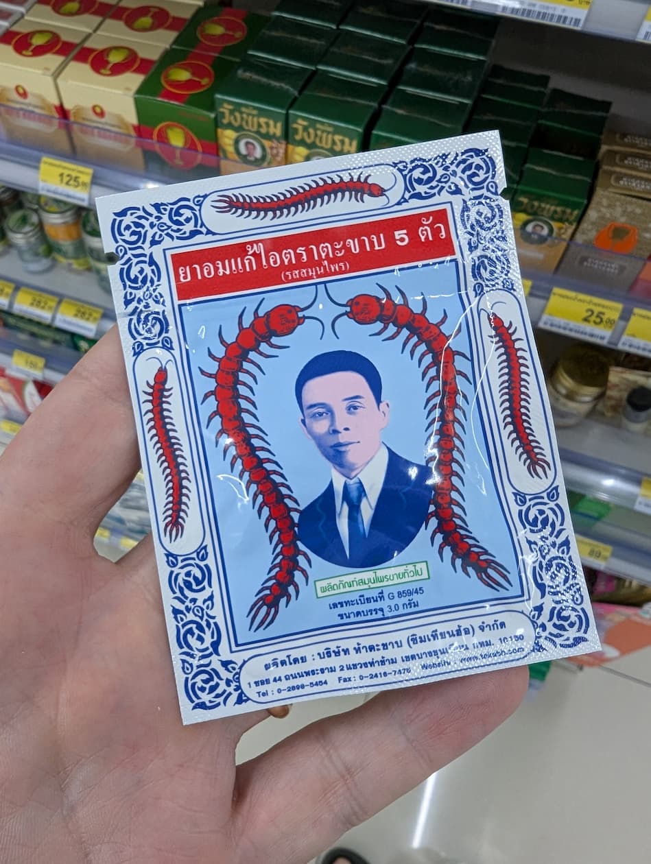 Person holding a white sachet of Takabb Anti-Cough Pills with centipede illustrations in a Thailand 7-Eleven