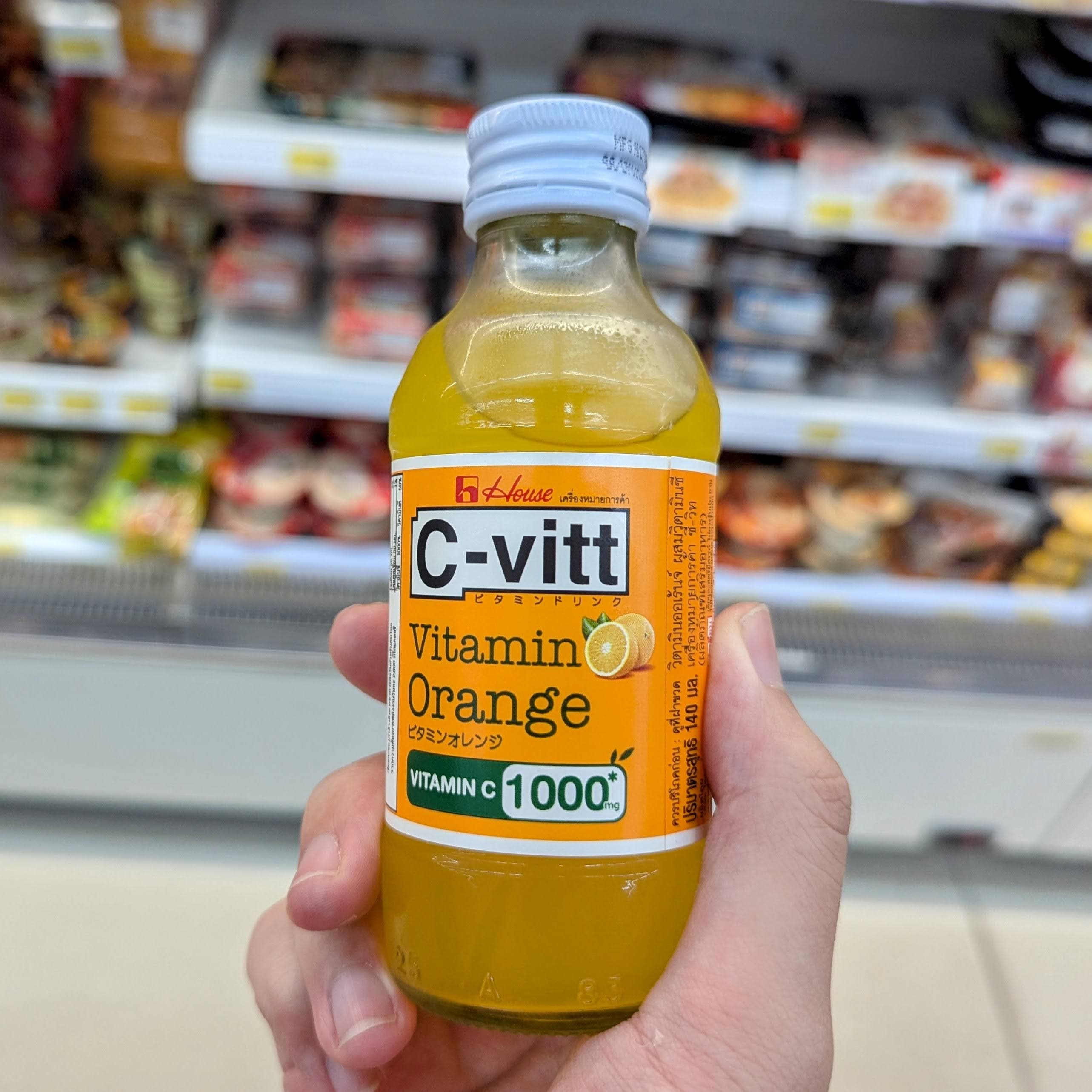 A small glass bottle of C-Vitt Orange vitamin drink in front of a 7-Eleven cooler in Thailand.