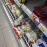 A refrigerated shelf at 7-Eleven Thailand showing bags of fresh 'Natural Veggies' including morning glory and cabbage.