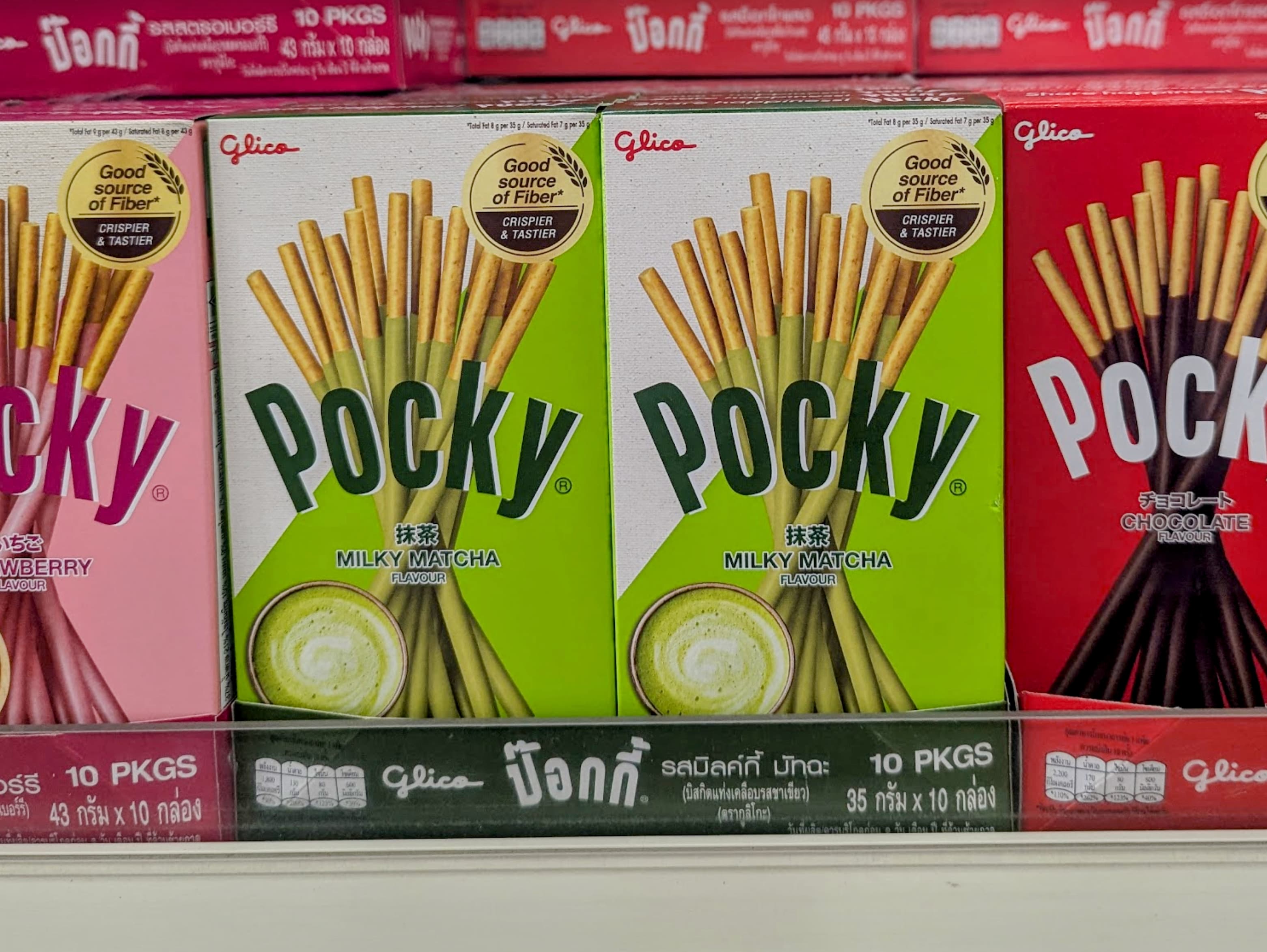 A box of Glico Pocky Milky Matcha being held against a bright 7-Eleven background in Thailand.