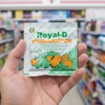 A sachet of Royal-D orange electrolyte powder being held in front of a 7-Eleven Thailand store.
