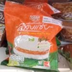 The 7-Eleven Survival Kit: 10 Must-Buy Items for Your First Day in Thailand A close-up of a toasted Basil Beef Sticky Rice burger from 7-Eleven Thailand being held in its plastic wrapper.