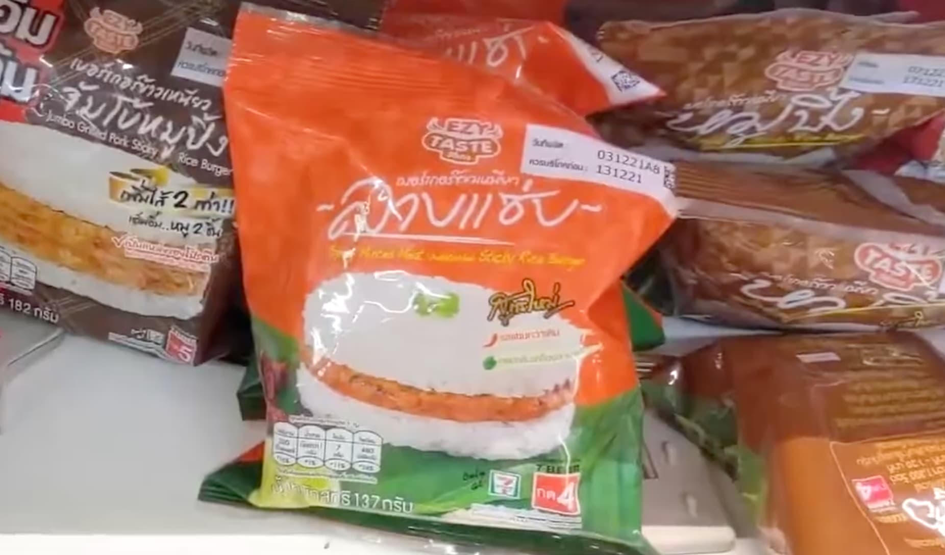 A close-up of a toasted Basil Beef Sticky Rice burger from 7-Eleven Thailand being held in its plastic wrapper.
