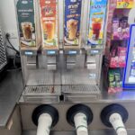 A row of self-serve drink dispensers at 7-Eleven Thailand featuring Espresso, Thai Tea, Latte, and Nestea Lemon.