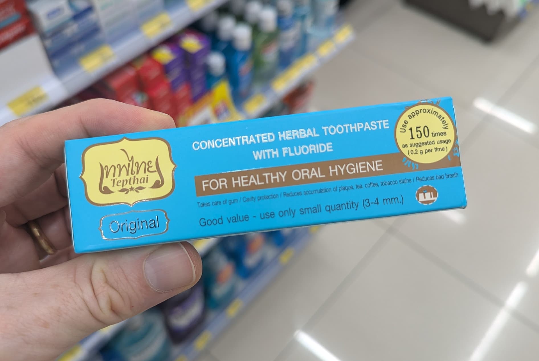 A hand holding a blue box of Tepthai Concentrated Herbal Toothpaste in a 7-Eleven Thailand aisle.