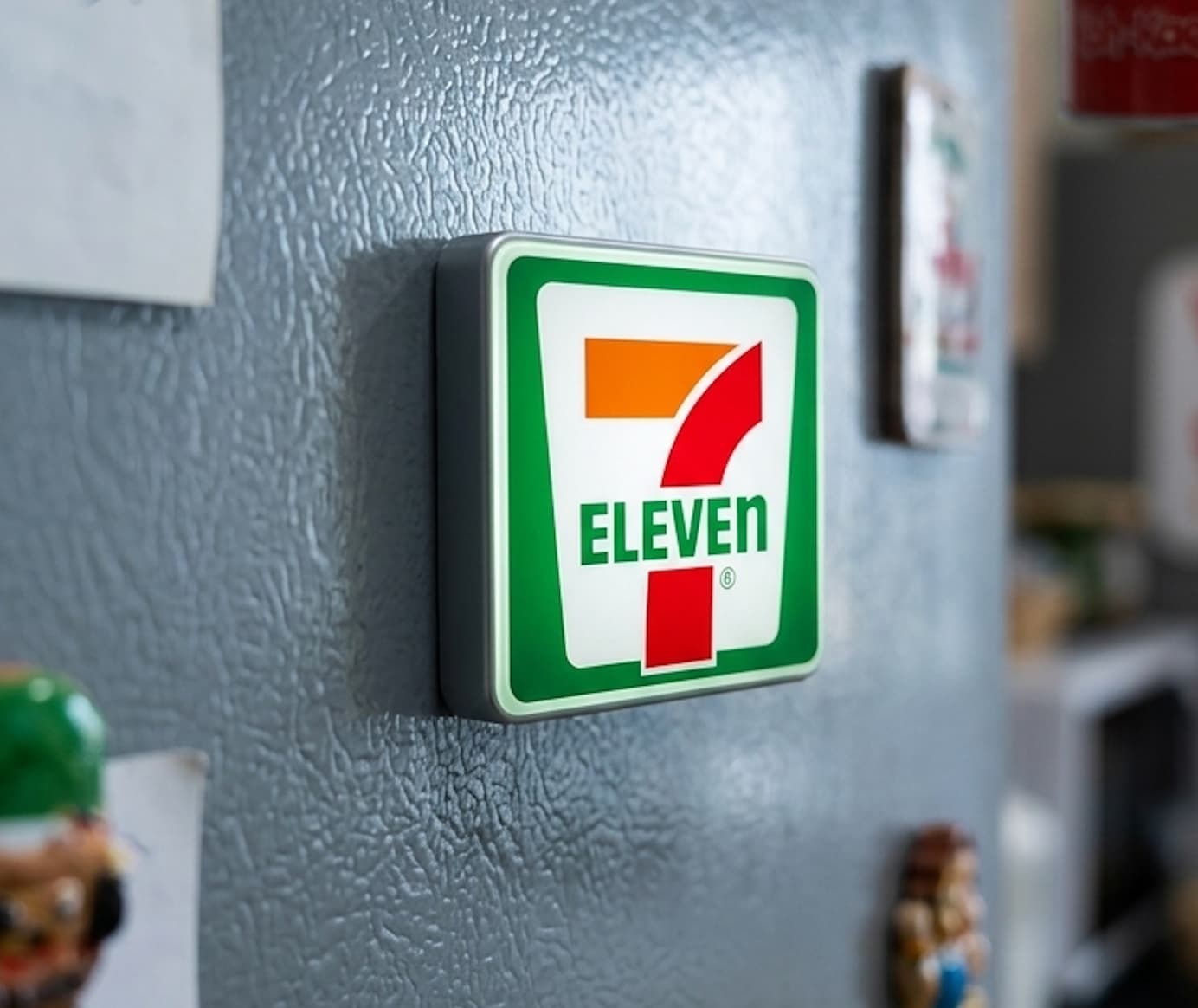 A detailed miniature 7-Eleven fridge magnet with LED lights glowing.