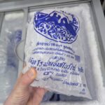 Nazzly Lively Nose Premium: The Most Aggressive (and Satisfying) Pore Strip in 7-Eleven A hand holding a traditional white and blue 1kg bag of standard tube ice inside a 7-Eleven freezer chest in Thailand.