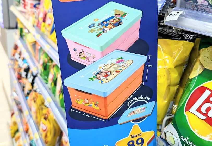 A blue vertical promotional display sign for the 7-Eleven ALL Member Crayon Shin-chan collapsible storage boxes on a store shelf in Thailand.