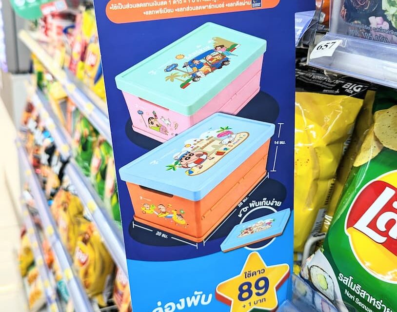 A blue vertical promotional display sign for the 7-Eleven ALL Member Crayon Shin-chan collapsible storage boxes on a store shelf in Thailand.