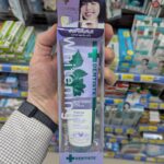 A hand holding a box of Dentiste' Whitening Purple Toothpaste featuring Lisa from Blackpink inside a store in Thailand.