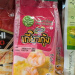 A hand holding a pink plastic pouch packaging of Jade Dragon Shrimp Dumplings on a refrigerated store shelf in Thailand.