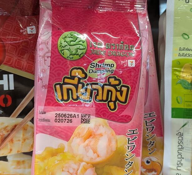 Jade Dragon Shrimp Dumpling: A Solid Emergency Fix That Can’t Compete with Fresh Markets A hand holding a pink plastic pouch packaging of Jade Dragon Shrimp Dumplings on a refrigerated store shelf in Thailand.