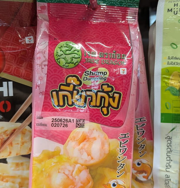 A hand holding a pink plastic pouch packaging of Jade Dragon Shrimp Dumplings on a refrigerated store shelf in Thailand.