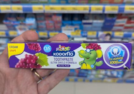 Kodomo Ultra Shield Cream Grape: An Overly Sweet, Artificial Paste That Misses the Mark A hand holding a purple box of Kodomo Toothpaste Ultra Shield Formula in Cream Grape flavor inside a store in Thailand.
