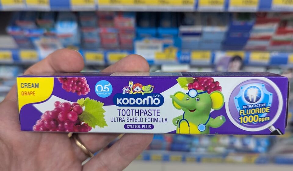 Kodomo Ultra Shield Cream Grape: An Overly Sweet, Artificial Paste That Misses the Mark A hand holding a purple box of Kodomo Toothpaste Ultra Shield Formula in Cream Grape flavor inside a store in Thailand.