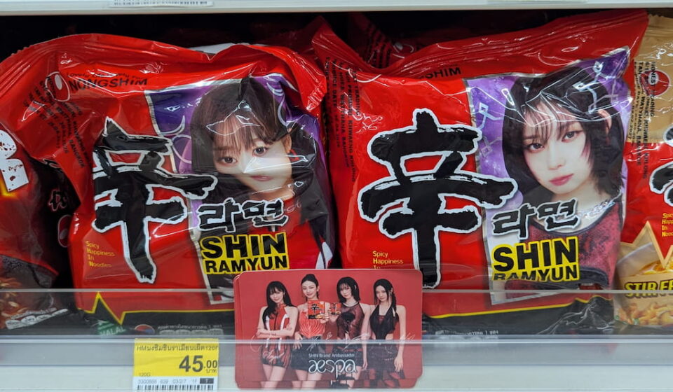 Nongshim Shin Ramyun Aespa Edition: The Undisputed King of Korean Instant Noodles Red packaging packets of Nongshim Shin Ramyun instant noodles featuring Aespa members on a 7-Eleven store shelf in Thailand.