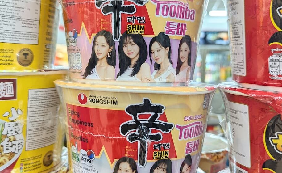 Nongshim Shin Ramyun Toomba Aespa Edition: A Silky, Creamy Twist on Legendary Korean Heat Yellow and cream insulated instant noodle bowls of Nongshim Shin Ramyun Toomba featuring K-pop group Aespa on a store shelf in Thailand.