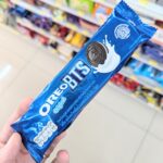 Makado Sticks Barbecue: The Ultimate No-Nonsense Beer Companion A hand holding a blue metallic plastic tube packaging of limited edition Oreo Original BTS cookies inside a store in Thailand.