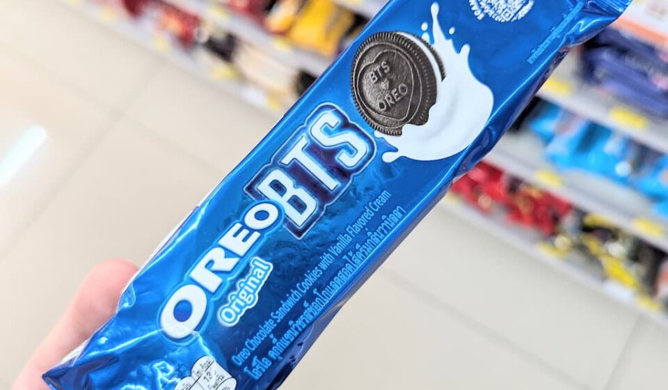 A hand holding a blue metallic plastic tube packaging of limited edition Oreo Original BTS cookies inside a store in Thailand.