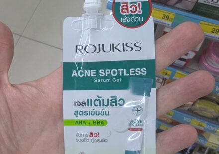 Rojukiss Acne Spotless Serum Gel: High-Quality Korean Skincare in a Pocket-Sized Sachet A hand holding a white and green sachet of Rojukiss Acne Spotless Serum Gel with a screw cap inside a store in Thailand.