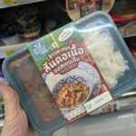 Sappe Beauti Drink: The Sweet Illusion of Convenience Store Wellness A premium black plastic tray with a red sleeve of Ros'niyom Australian Chuck Beef Red Curry with Rice from 7-Eleven Thailand.