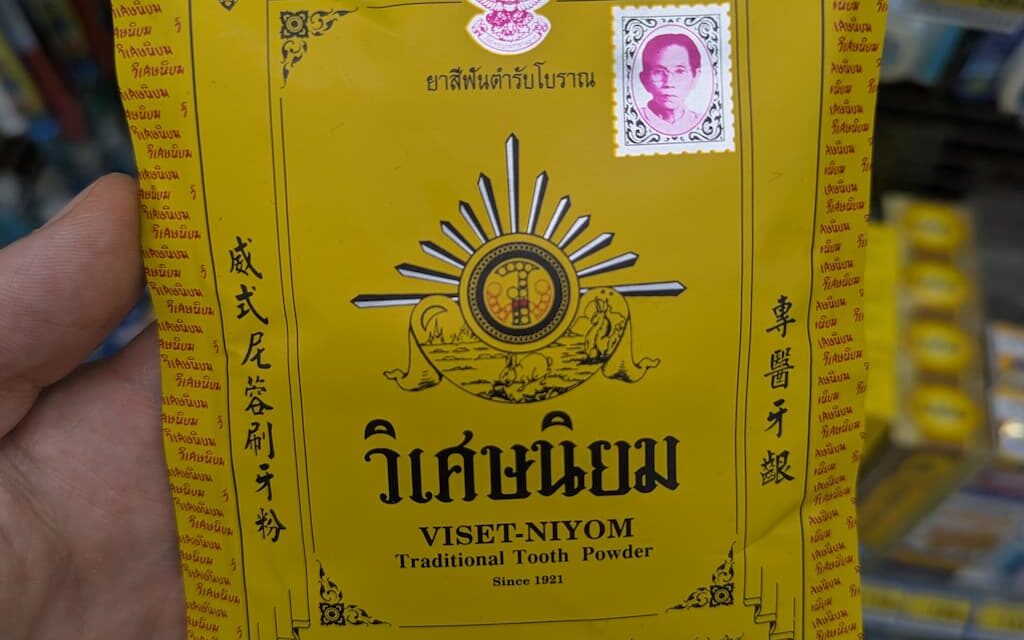A hand holding a yellow vintage paper envelope packet of Viset-Niyom Traditional Tooth Powder inside a 7-Eleven store in Thailand.