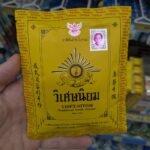 A hand holding a yellow vintage paper envelope packet of Viset-Niyom Traditional Tooth Powder inside a 7-Eleven store in Thailand.