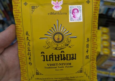 A hand holding a yellow vintage paper envelope packet of Viset-Niyom Traditional Tooth Powder inside a 7-Eleven store in Thailand.