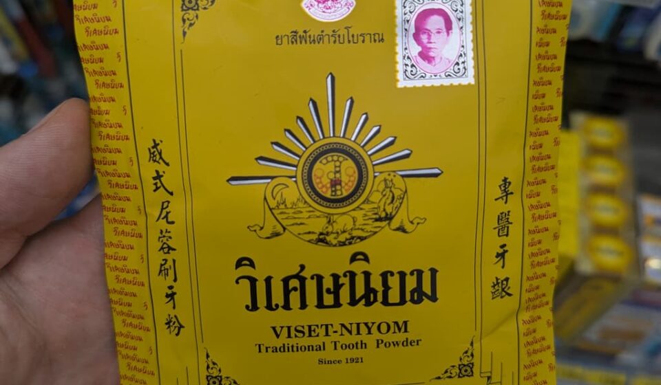 A hand holding a yellow vintage paper envelope packet of Viset-Niyom Traditional Tooth Powder inside a 7-Eleven store in Thailand.