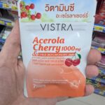 A hand holding a white and orange metallic zip-pouch of Vistra Acerola Cherry 1000mg dietary supplement tablets inside a store in Thailand.