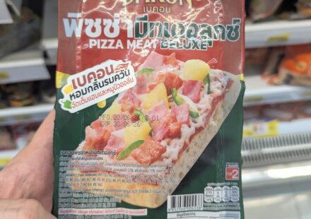 Bakon Pizza Meat Deluxe: A Mediocre, Soggy Fix for Late-Night Western Cravings A hand holding a dark green and red packaging pouch of a Bakon Pizza Meat Deluxe individual slice inside a store in Thailand.