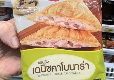 Ezygo Carbonara Danish Sandwich: A Flaky, Flawless Pastry Comfort Marvel A hand holding a light green and white plastic pouch packaging of an Ezygo Carbonara Danish Sandwich in front of store display shelves in Thailand.