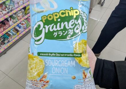 Grainey Popchip Multigrain Sourcream & Onion: A Light, Guilt-Free Snack That Scores on Subtle Flavor A hand holding a light blue bag of Grainey Popchip Multigrain Sourcream & Onion inside a 7-Eleven store in Thailand.
