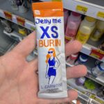 Ezygo Hawaiian Pizza Sandwich: A Crispy Toastie Weighed Down by Excessive Sweetness A hand holding a silver and orange single-serve stick pouch of HandyHerb Jelly Me XS Burin L-Carnitine on a store shelf in Thailand.