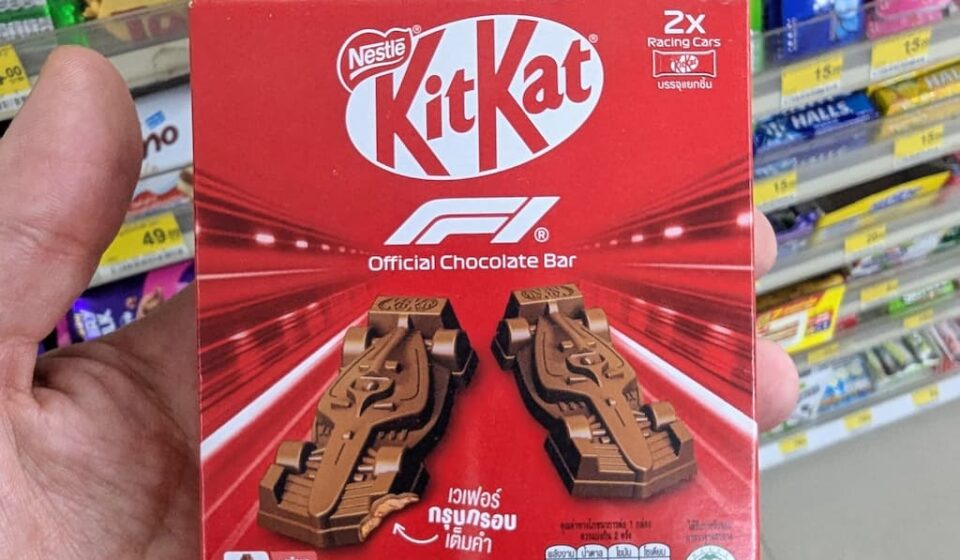 KitKat F1 Official Chocolate Bar: An Elite Racing-Themed Novelty That Delivers Outstanding Flavor A hand holding a red box of KitKat F1 Official Chocolate Bar featuring two molded chocolate racing cars inside a 7-Eleven in Thailand.