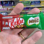 Monchhichi x Amaze One Tech Accessories: Flashy Character Power Banks and Gadgets with Niche Appeal A hand holding a green KitKat x Milo single wafer chocolate bar inside a 7-Eleven store in Thailand.