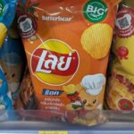 Lay’s Rock Chili & Salt: A Sharp, Artificial Kick That Needs a Cold Brew Companion An orange packaging bag of Lay's Rock Charcoal BBQ flavor potato chips resting on a 7-Eleven store display shelf in Thailand.