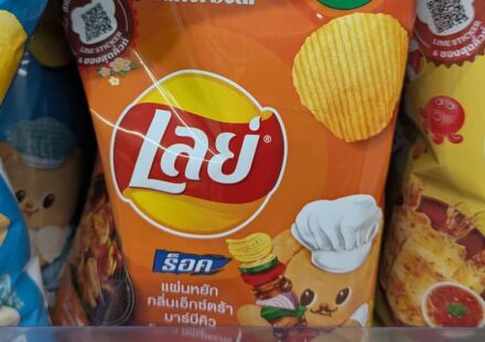 An orange packaging bag of Lay's Rock Charcoal BBQ flavor potato chips resting on a 7-Eleven store display shelf in Thailand.