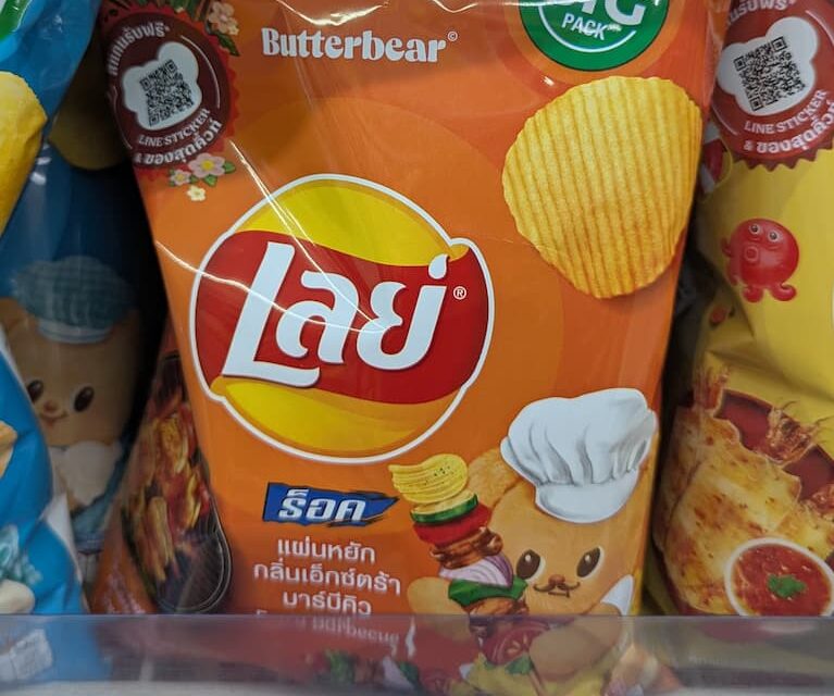An orange packaging bag of Lay's Rock Charcoal BBQ flavor potato chips resting on a 7-Eleven store display shelf in Thailand.