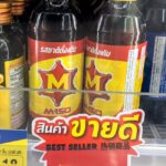 Can You Get a Thailand eSIM at 7-Eleven? (What You Need to Know Before You Walk In) Two glass bottles of M-150 Original energy and vitamin drink behind a yellow 10-Baht price tag on a 7-Eleven store shelf in Thailand.