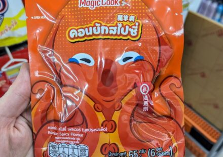 A hand holding an orange pouch of Magic Cook Konjac Spicy Flavour by Haidilao featuring a cartoon octopus inside a 7-Eleven in Thailand.