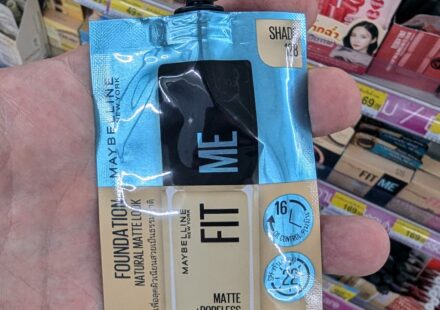 Maybelline Fit Me Matte + Poreless Foundation Sachet (Shade 128): Convenient Western Classic Facing Tough K-Beauty Competition A hand holding a Maybelline Fit Me Matte + Poreless Foundation sachet in Shade 128 inside a 7-Eleven store in Thailand.