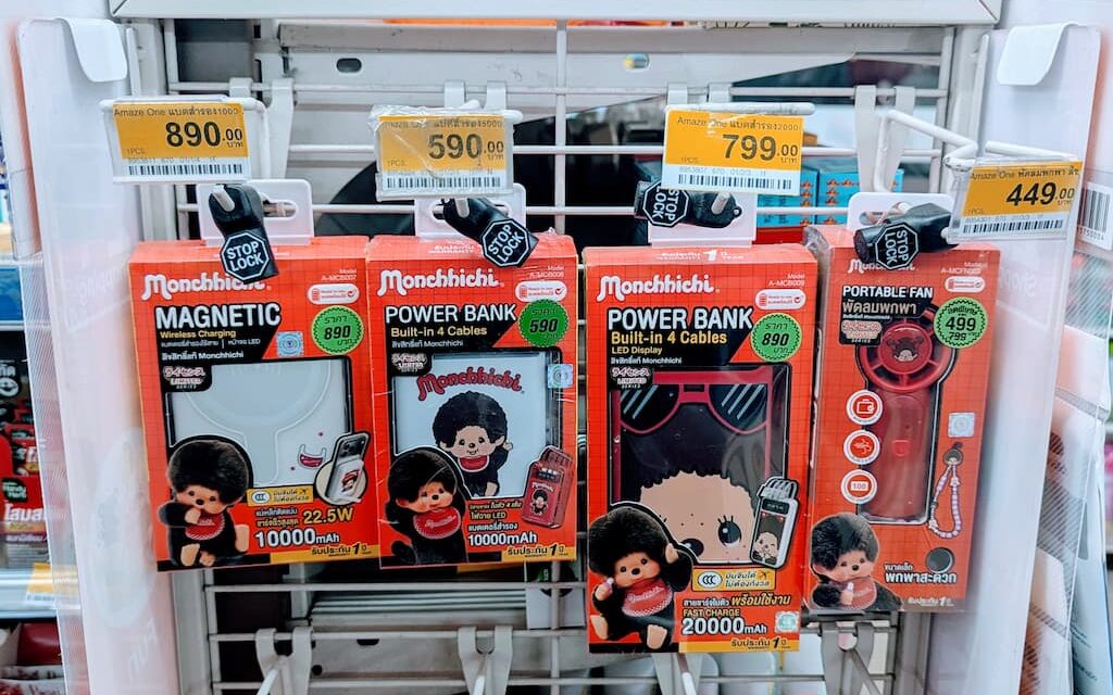 A white display rack filled with red box Monchhichi x Amaze One power banks and tech accessories inside a 7-Eleven store in Thailand.