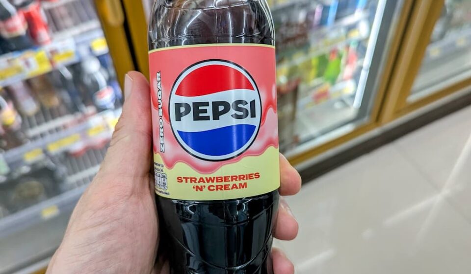 Pepsi Strawberries ‘N’ Cream Zero Sugar: A Bold Dessert Fusion Limited by Overwhelming Sweetness A hand holding a clear plastic bottle of Pepsi Strawberries 'N' Cream Zero Sugar soda with a pink cap inside a 7-Eleven store in Thailand.