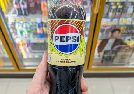 A hand holding a green-capped bottle of Pepsi Zero Sugar Dubai Chocolate flavor inside a 7-Eleven store in Thailand.