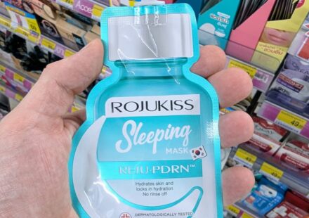 A hand holding a turquoise pouch of Rojukiss Reju-PDRN Sleeping Mask inside a 7-Eleven store in Thailand.