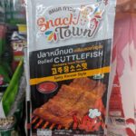 A hand holding a white and orange pouch of Snack Town Rolled Cuttlefish Gochujang Sauce Flavour inside a 7-Eleven in Thailand.