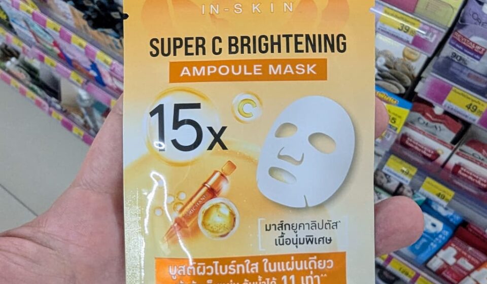 A hand holding a yellow sachet of Srichand In-Skin Super C Brightening Ampoule Mask inside a 7-Eleven store in Thailand.