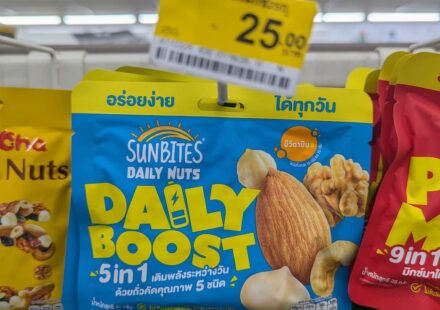 Sunbites Daily Nuts Daily Boost 5 in 1: Budget-Friendly Mixed Nuts with a Soft Texture Crunch A hand holding a blue pouch of Sunbites Daily Nuts Daily Boost 5 in 1 hanging on a 7-Eleven rack in Thailand with a 25 THB price tag above.