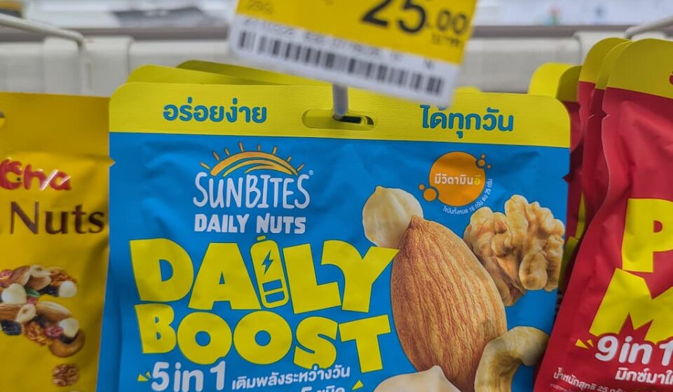 Sunbites Daily Nuts Daily Boost 5 in 1: Budget-Friendly Mixed Nuts with a Soft Texture Crunch A hand holding a blue pouch of Sunbites Daily Nuts Daily Boost 5 in 1 hanging on a 7-Eleven rack in Thailand with a 25 THB price tag above.